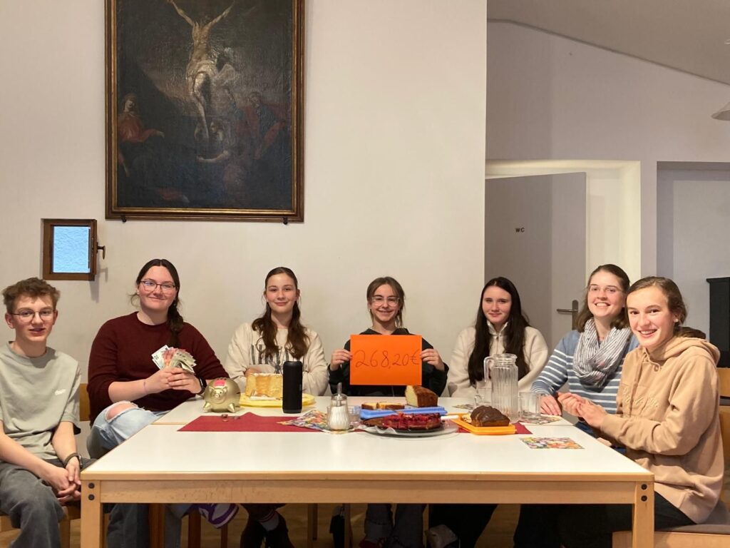 Die 6 Winkler Firmlinge und Angelika Kühnhauser sitzen gemeinsam am Tisch, es gibt Kuchen und etwas zu trinken. Der Firmling, der in der Mitte sitzt hält ein Blatt mit der Höhe des Spendenbetrags: 268,20 €
