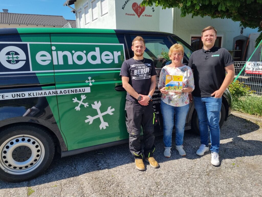Christian Einöder und ein Mitarbeiter der Firma stehen zusammen mit Rosmarie Baumgartner (1. Vorsitzende Kinderkrebshilfe BGL+TS) vor dem Firmenwagen der Firma Einöder, auf dem Parkplatz vor dem Vereinsheim der Kinderkrebshilfe BGL+TS
