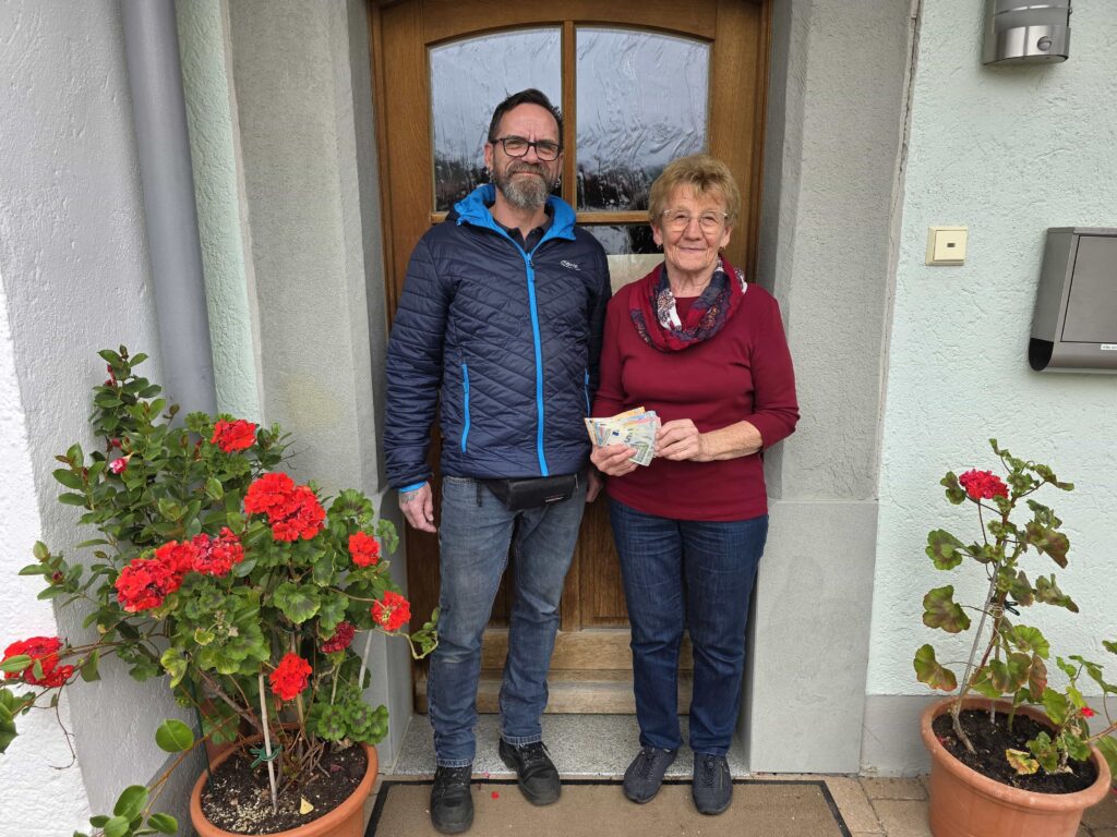 Herr Gollinger überreicht vor der Tür des Vereinsheims der Kinderkrebshilfe BGL+TS die Spende an Rosmarie Baumgartner.